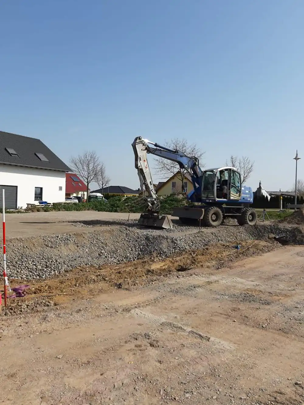 Bagger beim Anlegen eines Gründungspolsters auf einer Baustelle vor Wohnhäusern