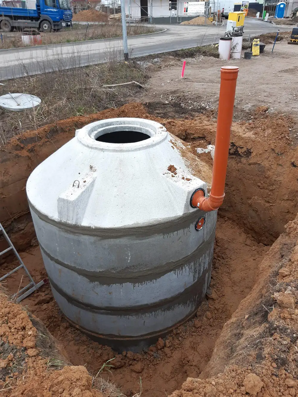 Einbau einer vollbiologischen Kläranlage aus Beton mit orangefarbenem Rohranschluss